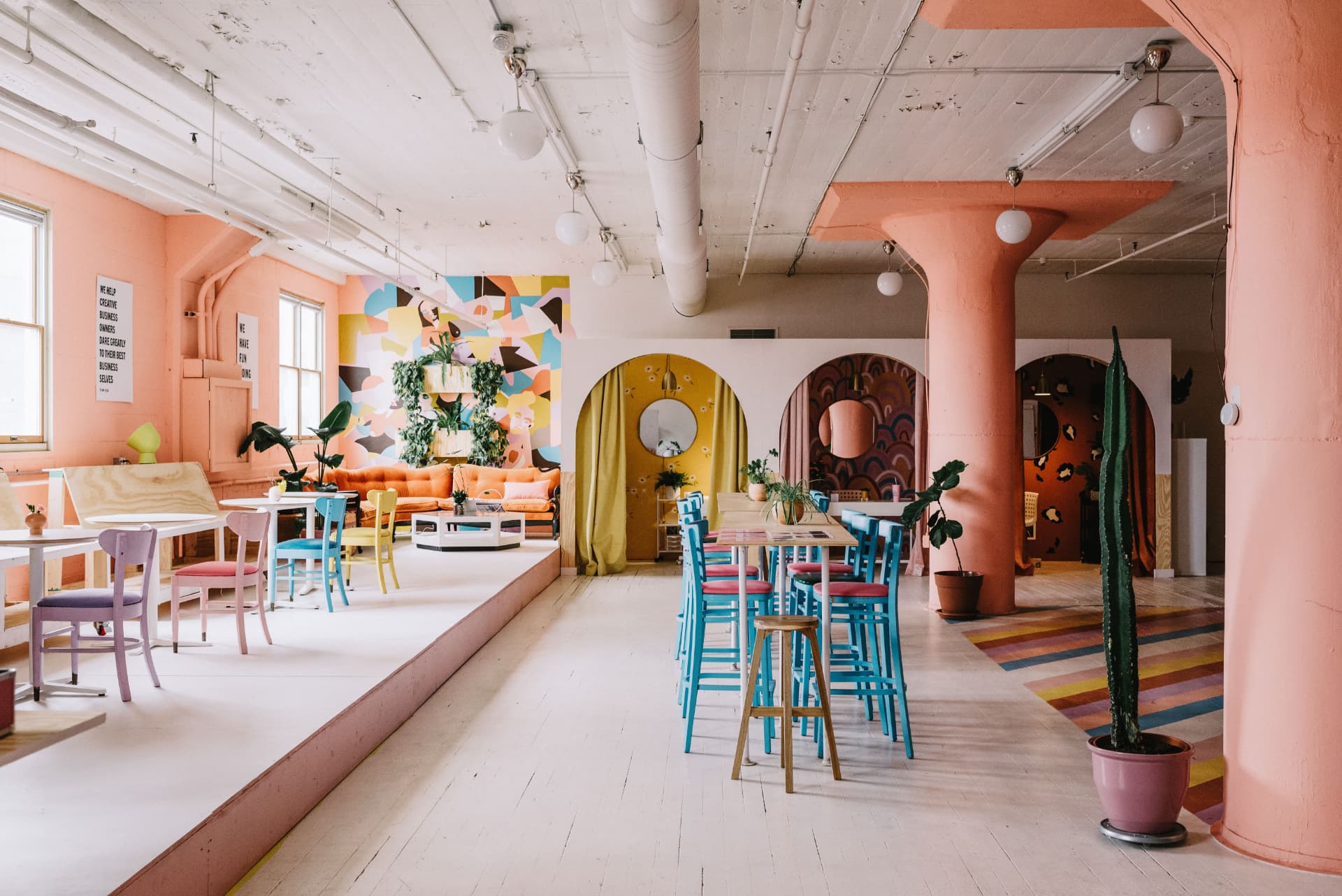 Pink and pastel event space with colorful mural, arched nooks and mismatched chairs