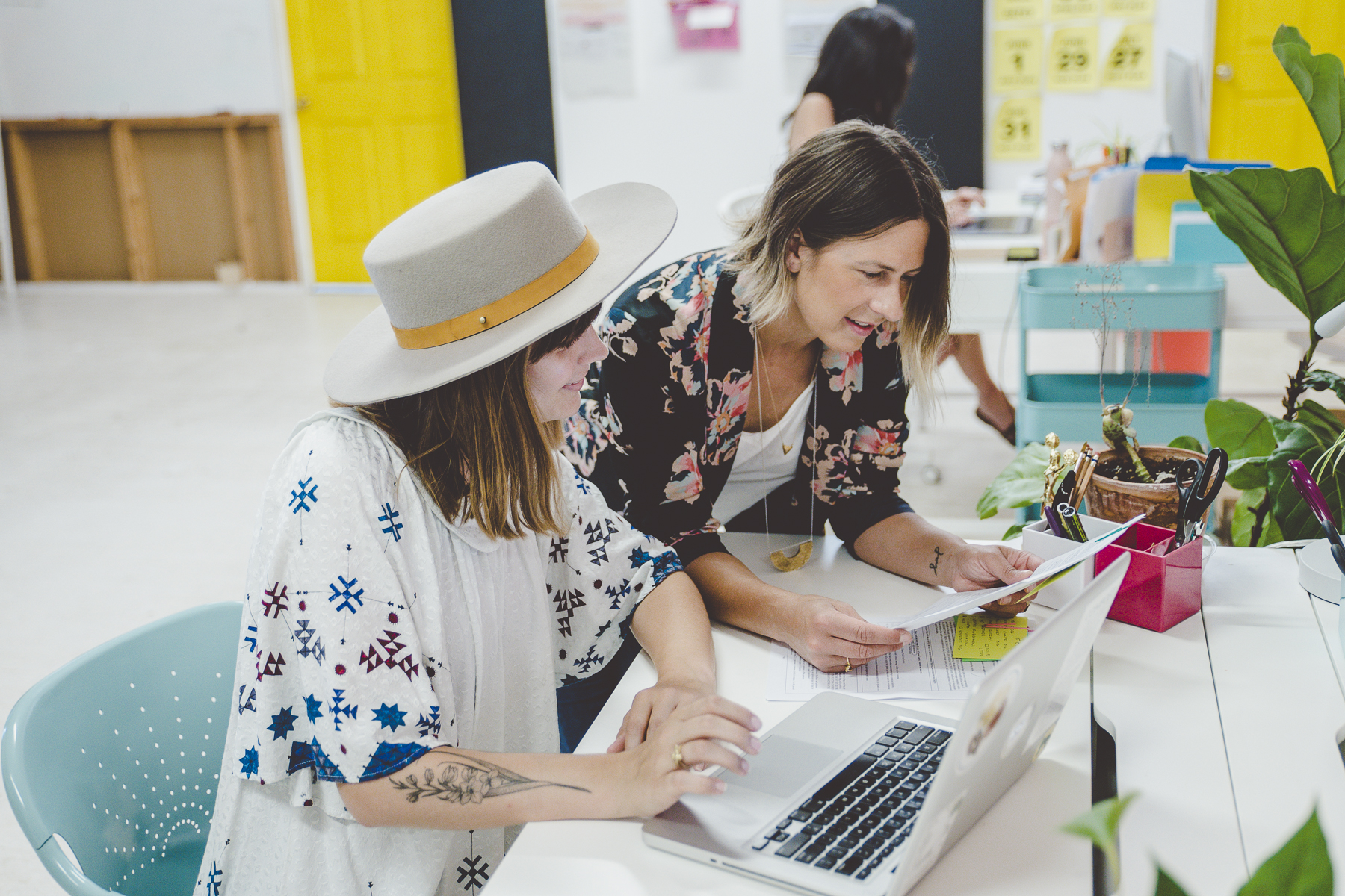 Two people reviewing printed pages and a laptop at a bright studio desk