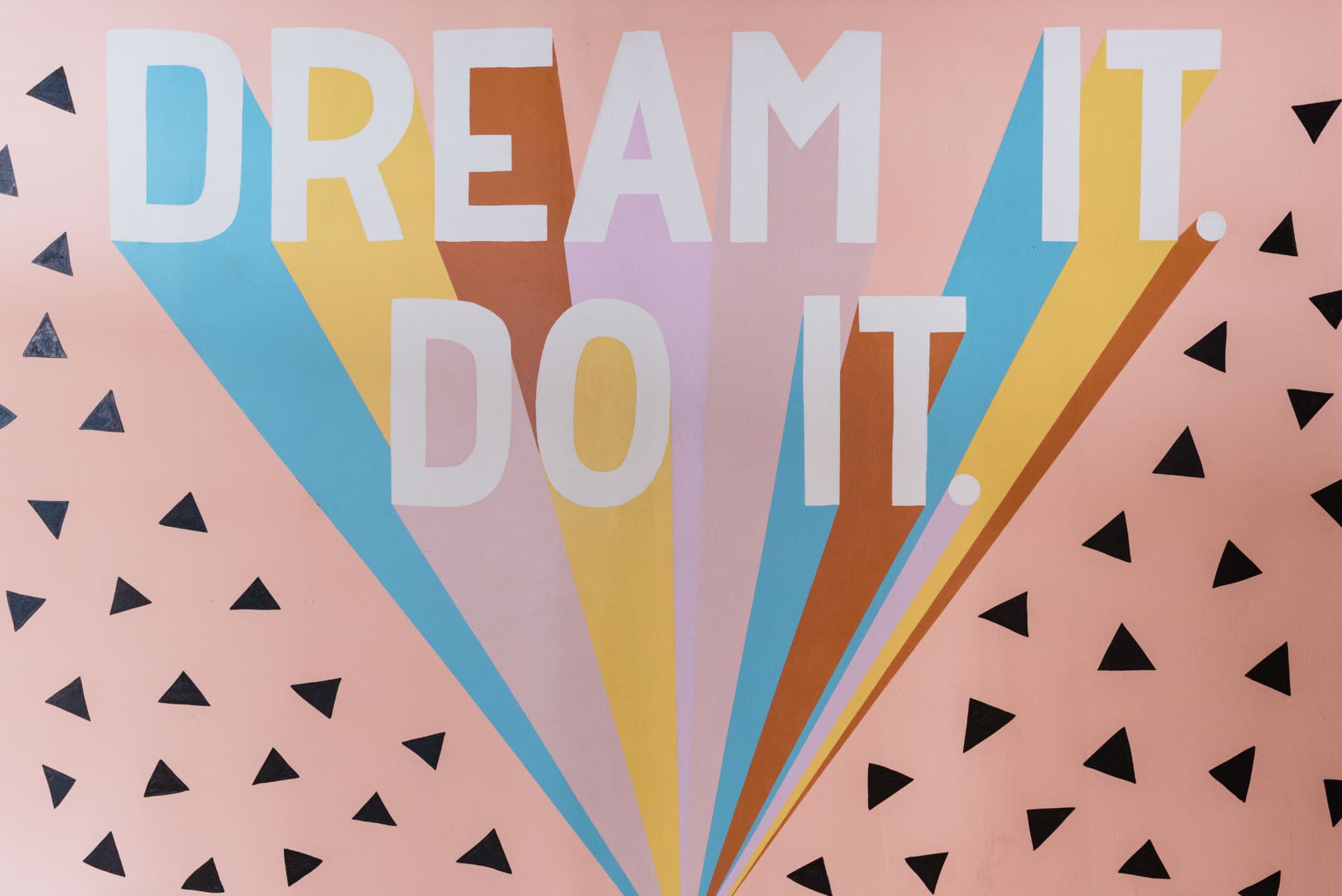 Colorful wall mural with bold 'DREAM IT DO IT' lettering and radiating geometric shapes